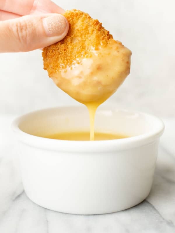 a female hand dipping a chicken nugget into honey mustard dipping sauce