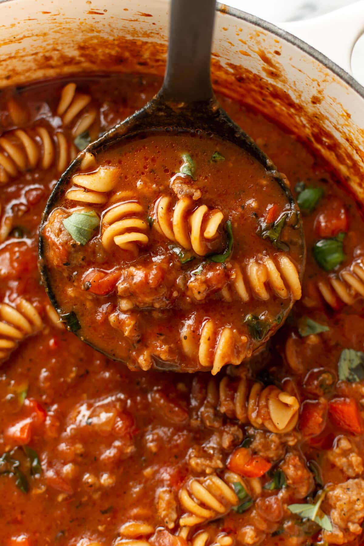 a dutch oven with italian sausage pasta soup and a ladle