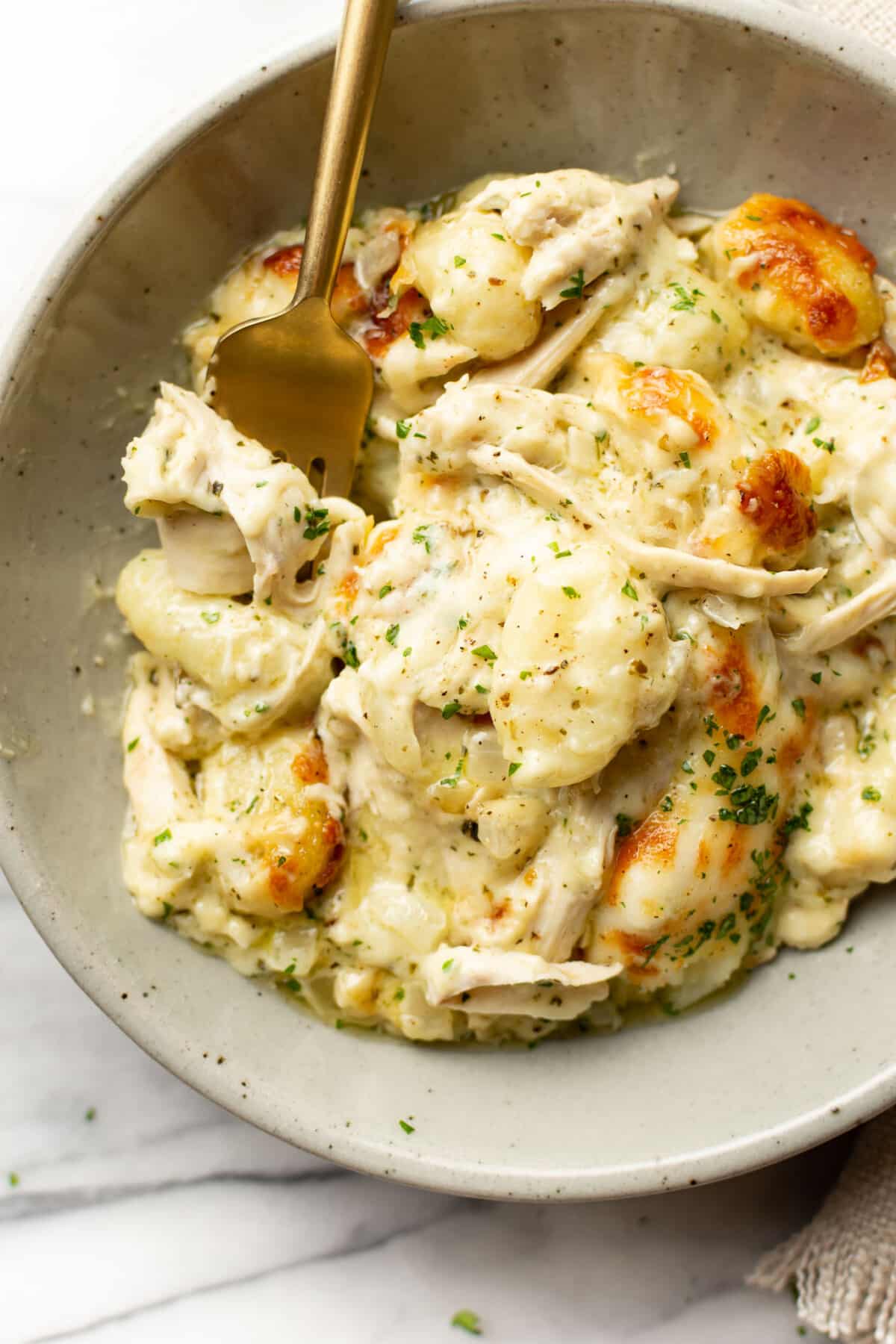 a bowl of baked chicken pesto gnocchi with a fork