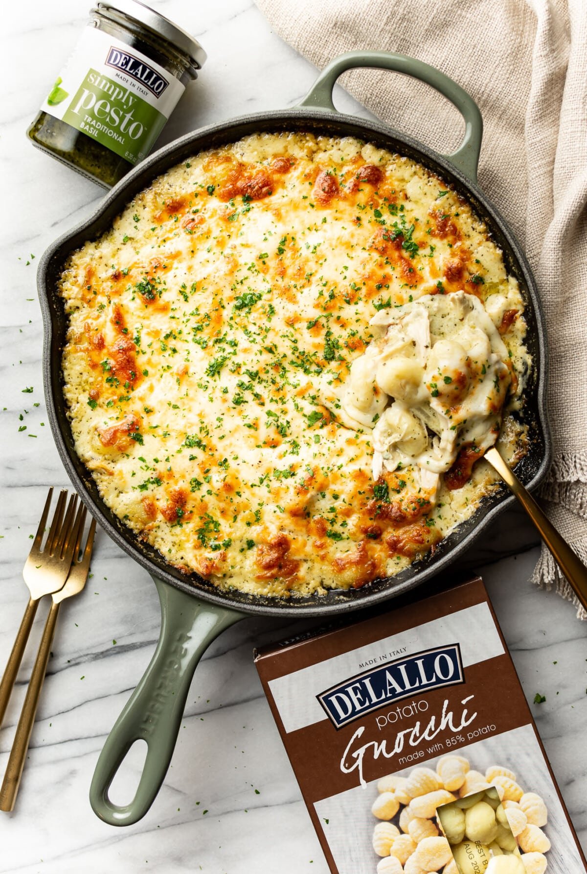 a skillet with baked chicken pesto gnocchi next o a jar of pesto and box of gnocchi