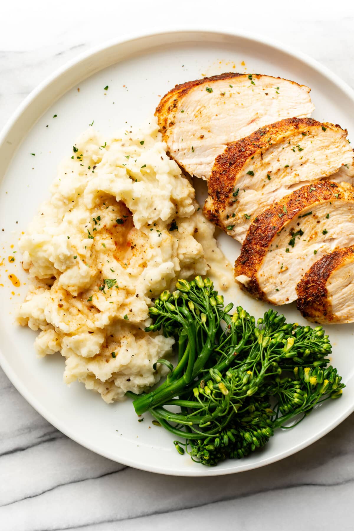 a plate with sliced air fryer chicken breast, mashed potatoes, and broccolini