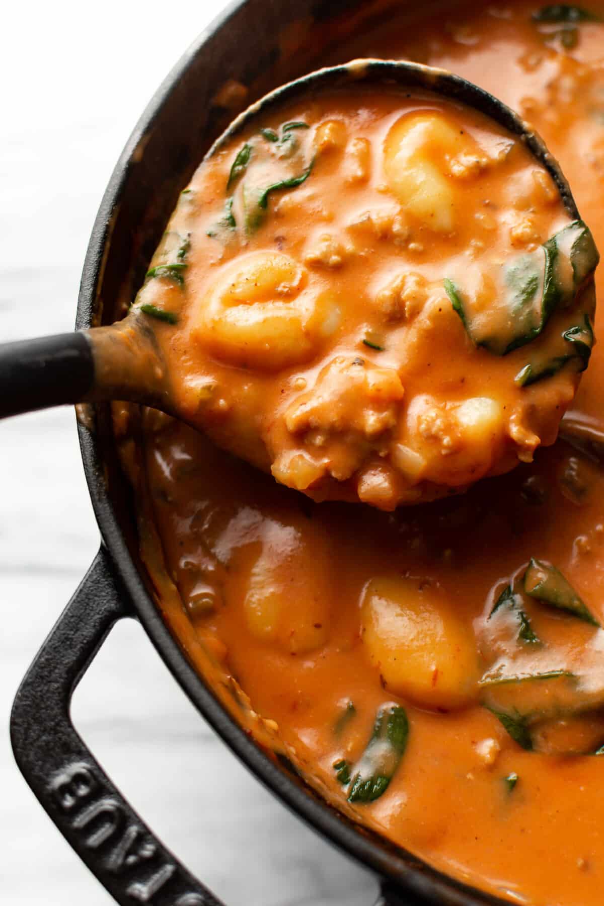 a dutch oven with a ladle of creamy italian sausage and gnocchi soup