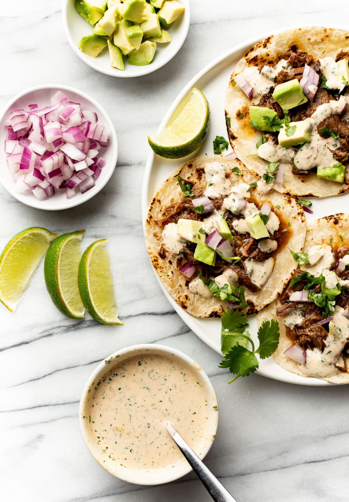 crockpot beef tacos next to bowls of toppings and chipotle dipping sauce