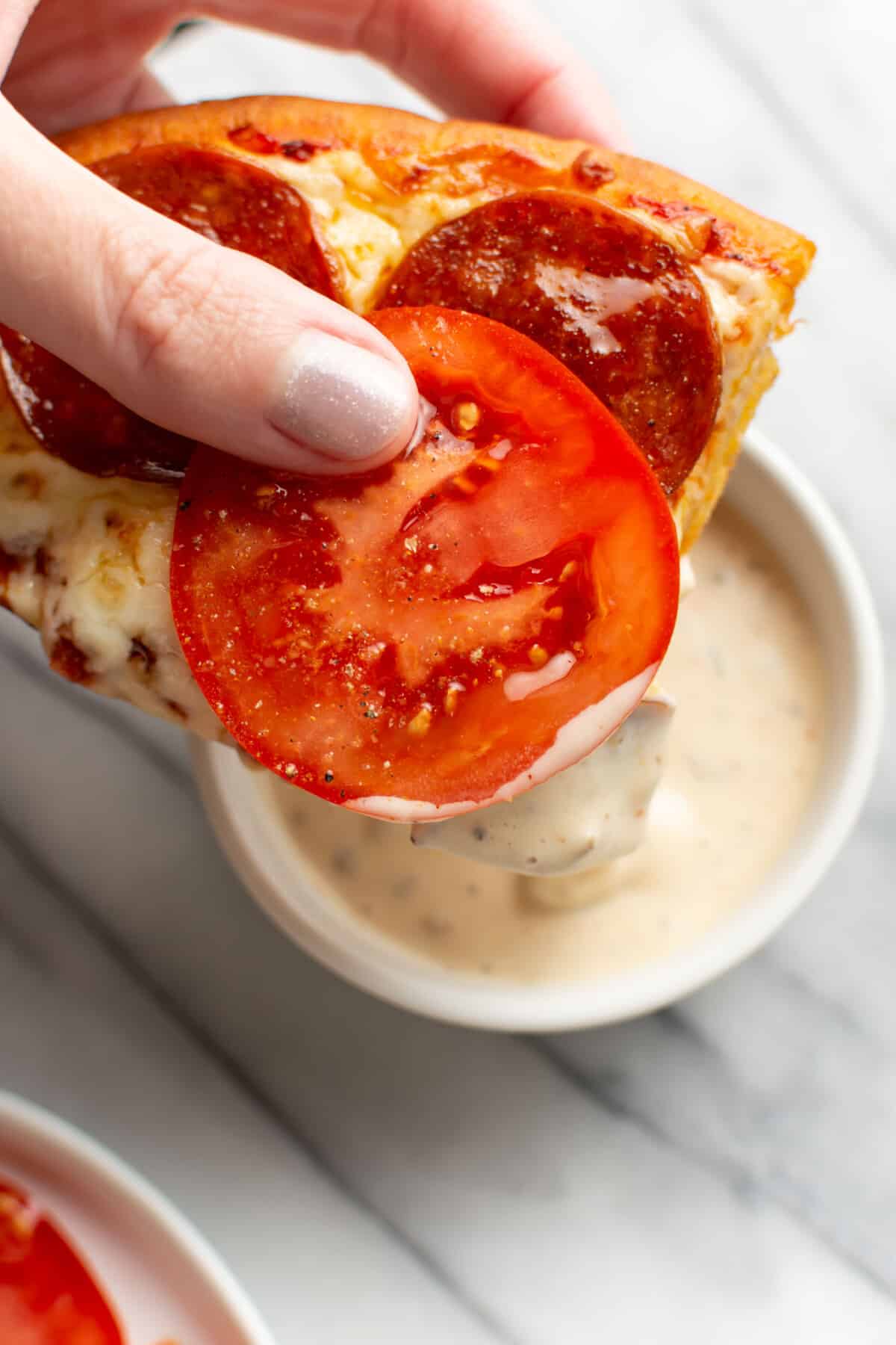 a female hand dipping a slice of naan pizza into dip