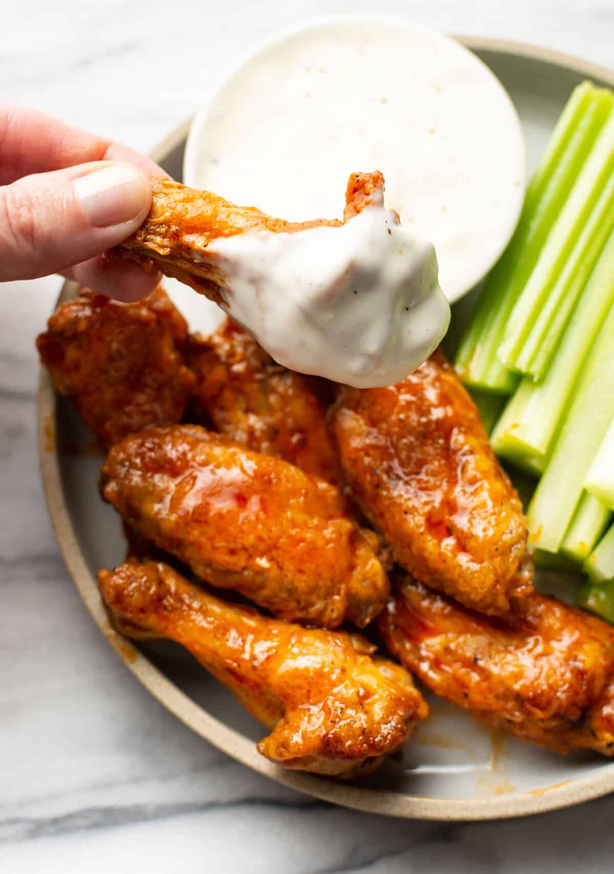 a female hand dipping an air fryer buffalo wing into ranch dip