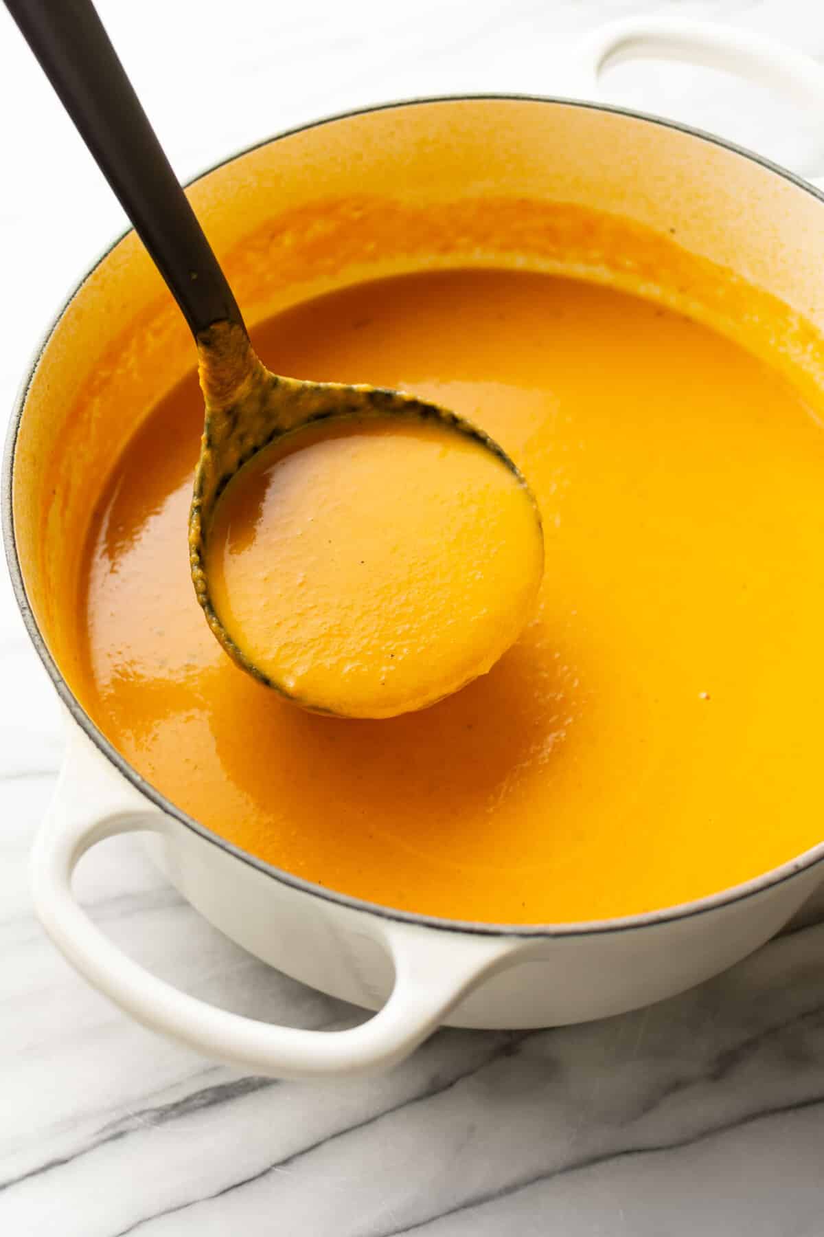 a pot of soup with carrot ginger soup and a ladle