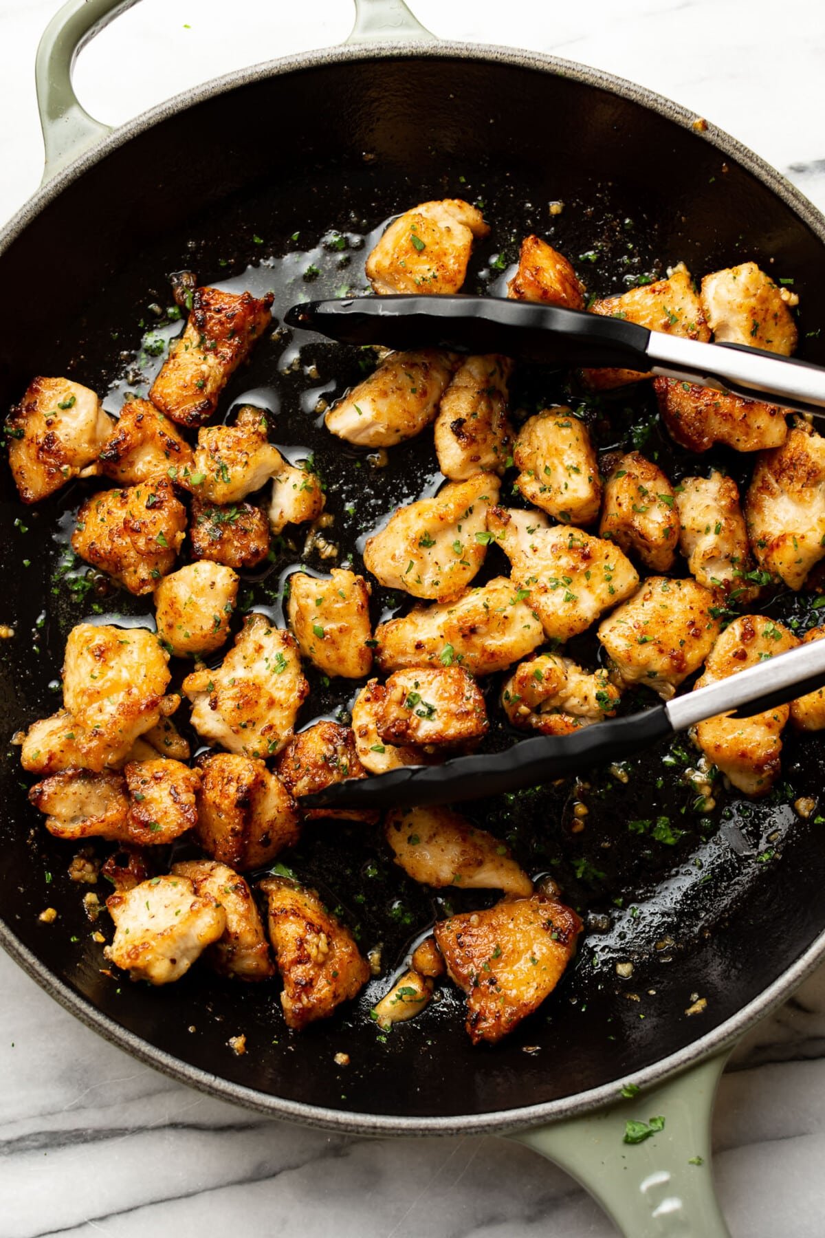 a skillet with garlic butter chicken bites and kitchen tongs