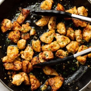 a skillet with garlic butter chicken bites and kitchen tongs