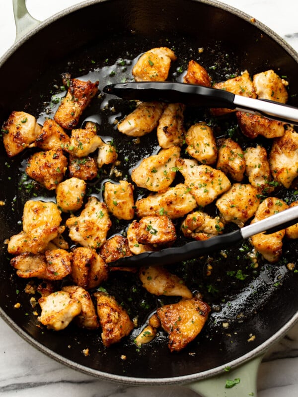 a skillet with garlic butter chicken bites and kitchen tongs