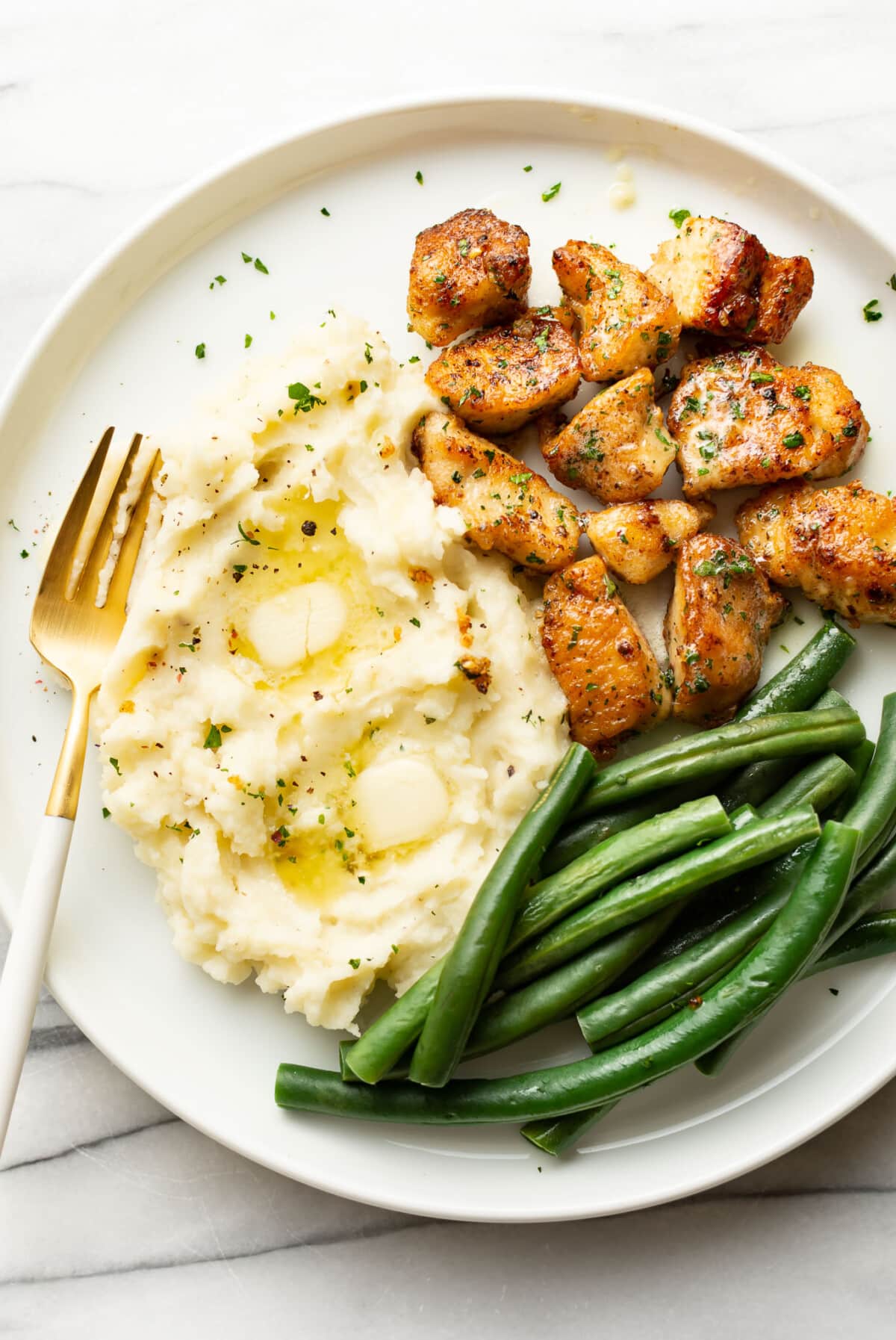 a plate with garlic butter chicken bites, mashed potatoes, and green beans