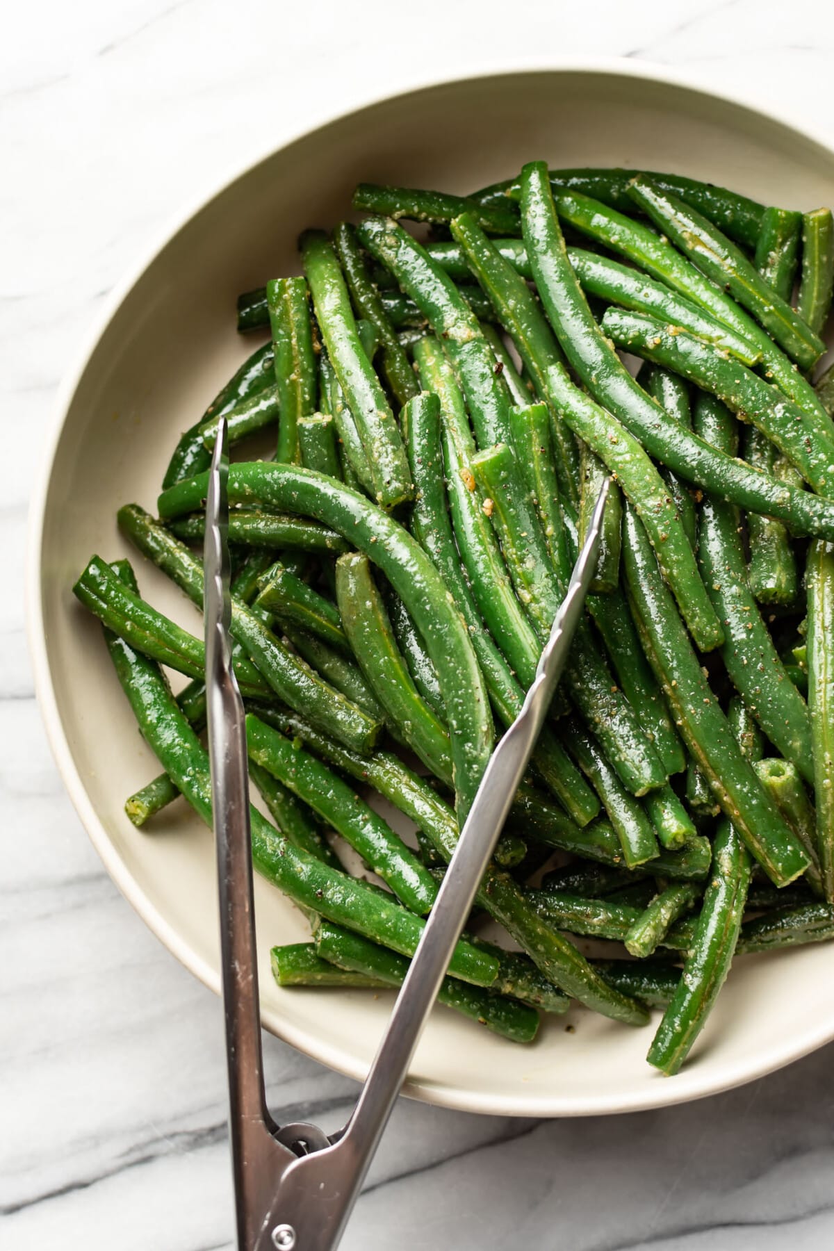 a bowl of sautéed green beans with serving tongs