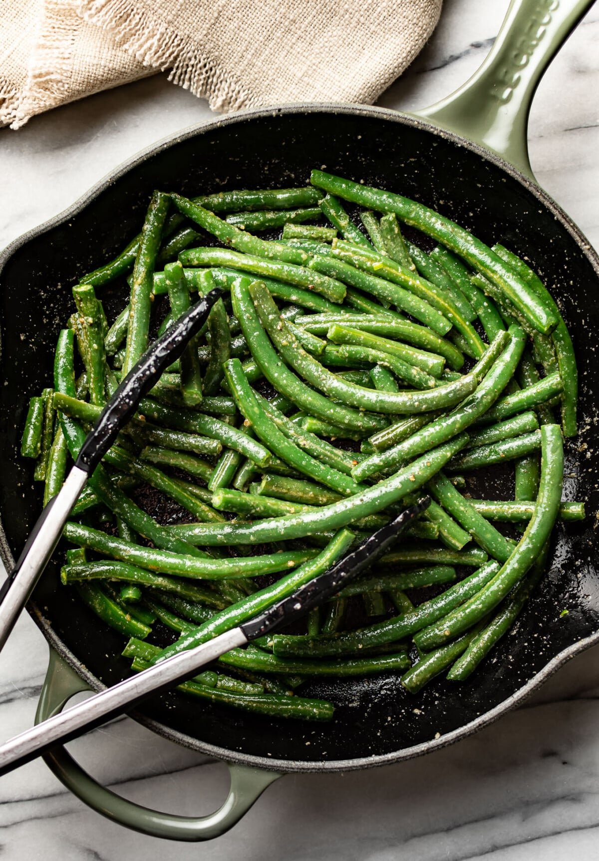 a skillet with sauteed green beans and cooking tongs