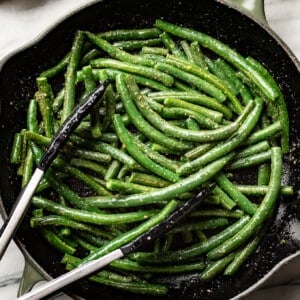 a skillet with sauteed green beans and cooking tongs