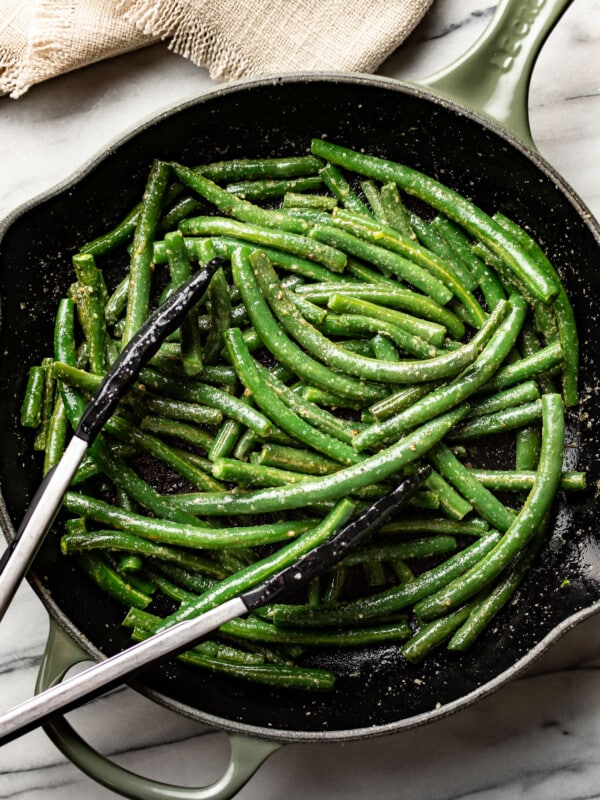 a skillet with sauteed green beans and cooking tongs