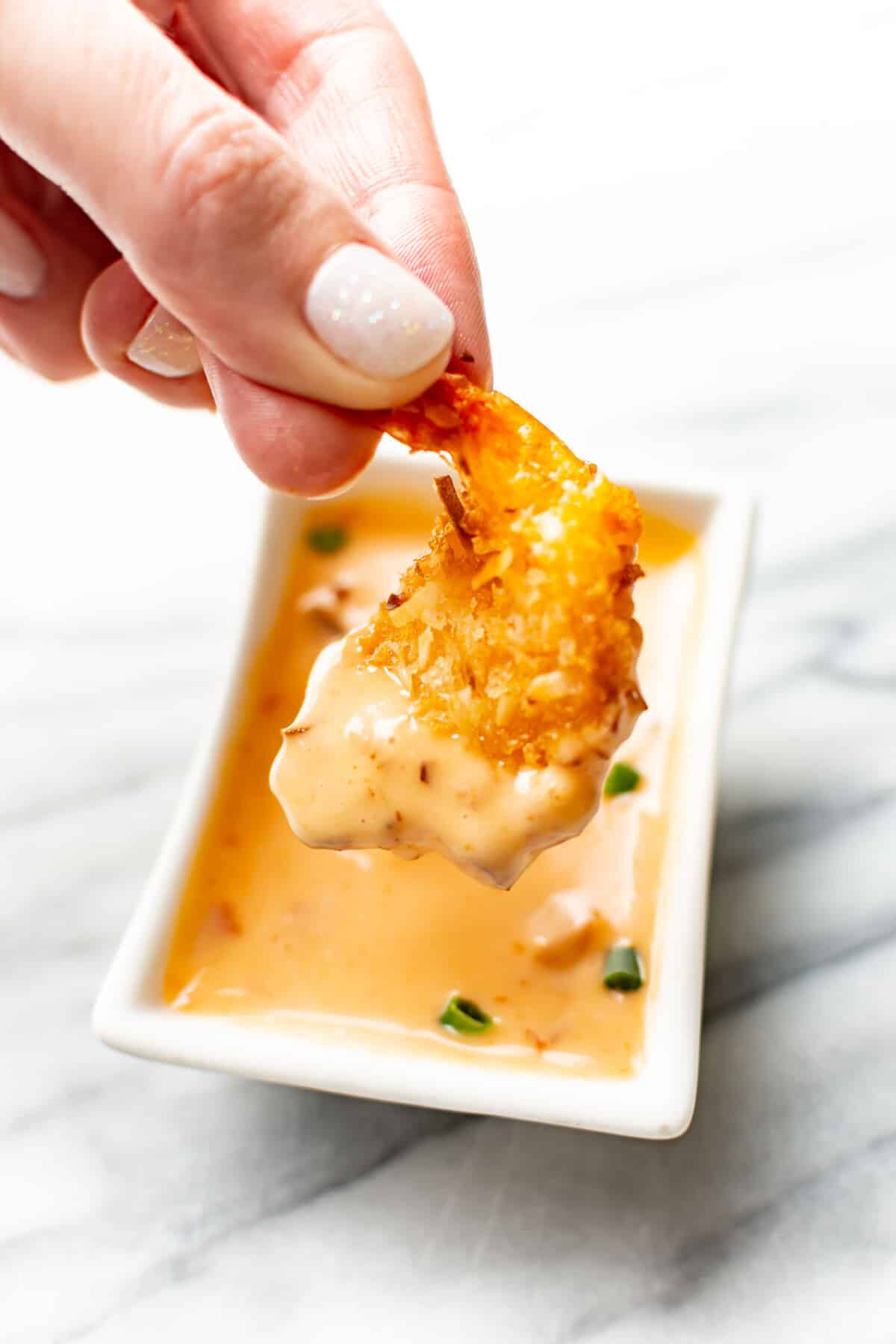 a female hand dipping a shrimp into homemade bang bang sauce