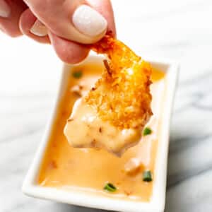 a female hand dipping a shrimp into homemade bang bang sauce