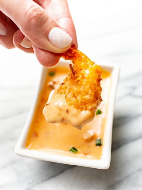 a female hand dipping a shrimp into homemade bang bang sauce